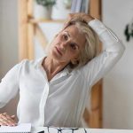 Woman stretching neck at a desk indoors