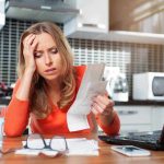 Woman looking stressed holding bills in kitchen