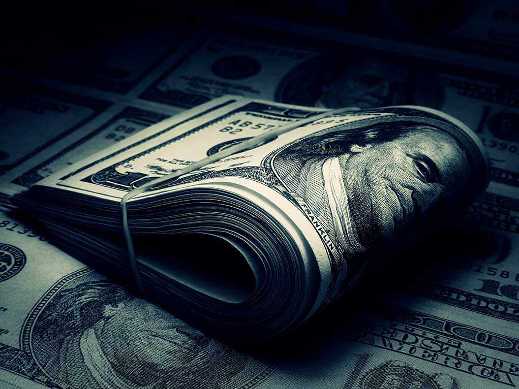 A rolled stack of hundred dollar bills on a background of more banknotes