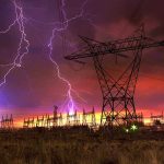 Lightning strikes illuminate a power station against a colorful sunset sky