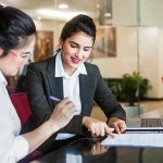 Two women discussing papers at a laptop