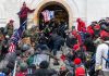 Crowd storming a building entrance with flags and signs