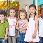 Five children standing together in a playground setting smiling at the camera