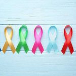 Colorful awareness ribbons on light wooden background.