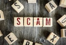 Wooden blocks spell SCAM on a rustic surface.