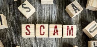 Wooden blocks spell SCAM on a rustic surface.