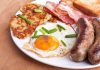 Bacon Without Pigs? Lab Breakthrough Stuns Meat Industry A hearty breakfast plate featuring a fried egg, crispy bacon, sausages, hash browns, and toasted bread garnished with green onions