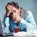 Man with tissue feeling unwell at laptop desk