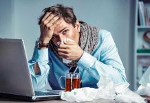 Man with tissue feeling unwell at laptop desk