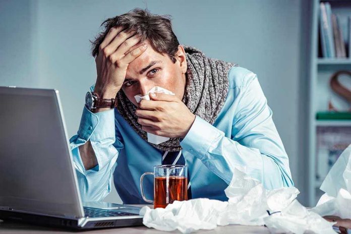 Man with tissue feeling unwell at laptop desk