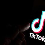 Finger pointing at TikTok logo on a screen.