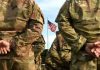 Soldiers stand in formation with American flag in background.