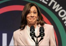 Adams SLAMS Kamala Harris—Maduro Hypocrisy Exposed Woman smiling behind two microphones on a podium.
