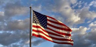 American flag waving against cloudy sky.