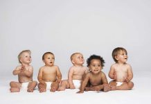 Five diverse babies sitting on a neutral background, displaying playful expressions