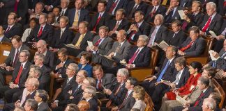 Audience of officials sitting and reading documents in auditorium.