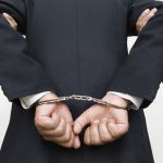 A person in a suit with hands cuffed behind their back
