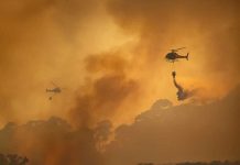 Helicopters dropping water over forest fire smoke sky