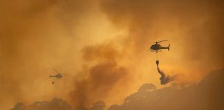 Helicopters dropping water over forest fire smoke sky