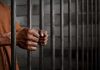 Hands gripping prison cell bars.