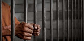 Hands gripping prison cell bars.
