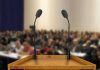 Unity Pitch Sparks Left-Right Backlash A wooden podium with two microphones in front of a blurred audience