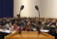 Unity Pitch Sparks Left-Right Backlash A wooden podium with two microphones in front of a blurred audience