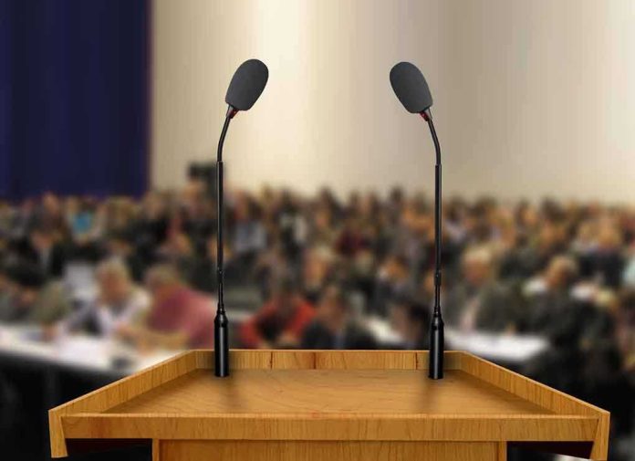 A wooden podium with two microphones in front of a blurred audience