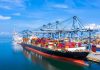 Two Tankers Blink—Prices Jump Container ship docked at a busy industrial port.