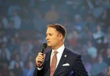 man in a suit speaking into a microphone on stage
