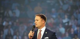 man in a suit speaking into a microphone on stage