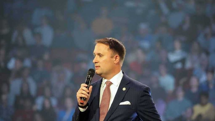 shutterstock_2374147685 man in a suit speaking into a microphone on stage