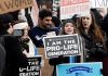 Power Shift: Doctor Overrules Boards Group of protesters holding pro-life signs at a rally