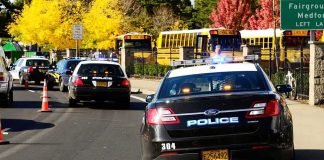 Police cars with flashing lights near school buses on a city street