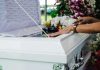hands resting on a white casket with flowers nearby