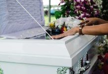 hands resting on a white casket with flowers nearby