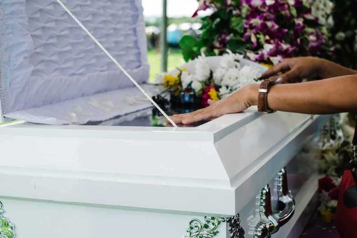 hands resting on a white casket with flowers nearby