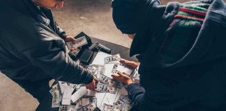 Triple-Digit Shock – The Iran Stat They Hide Two people sorting stacks of U.S. dollar bills on a table