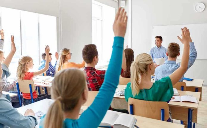 shutterstock_1470934406 Students raising hands in a classroom