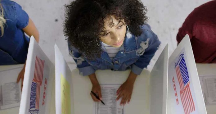 shutterstock_1737374783 Woman filling out ballot at a voting booth