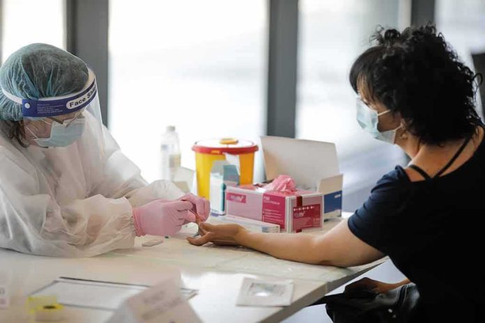 shutterstock_1754395331 Healthcare worker performs finger-prick test on masked patient