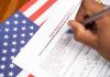 Hand filling out a voter registration form beside an American flag