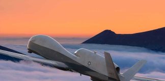 military drone flying above clouds at sunset