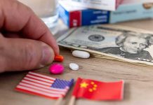 Hand picking an orange pill beside US and China flags and cash