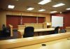 Killer Mom Avoids Prison—Here’s Why Interior view of an empty courtroom with wooden furniture and American flags