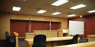 Interior view of an empty courtroom with wooden furniture and American flags