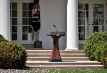 Cheesecake Quip Explodes Into Campaign Brawl Podium with presidential seal in a garden colonnade