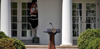 Cheesecake Quip Explodes Into Campaign Brawl Podium with presidential seal in a garden colonnade