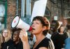Encampments Erased? Hilton Drops 2027 Bomb Woman with megaphone leading a protest