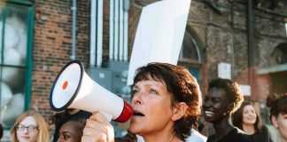 Encampments Erased? Hilton Drops 2027 Bomb Woman with megaphone leading a protest